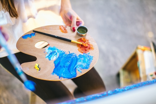 Artiste femme mélangeant des couleurs à l'huile sur palette tenant dans sa main