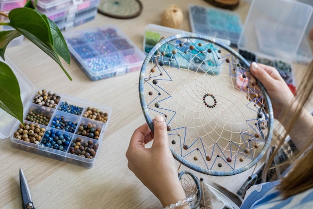 Une artiste en gros plan créant un accessoire fait main dreamcatcher utilise une amulette de perles colorées pour la chance