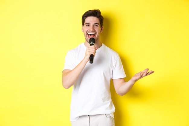 Un artiste heureux jouant, parlant dans un microphone, faisant un discours ou un spectacle debout, debout sur fond jaune