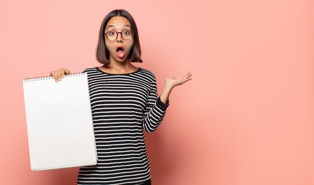 Artiste de la jeune femme à la surprise et choqué, avec la mâchoire tombée tenant un objet avec une main ouverte sur le côté