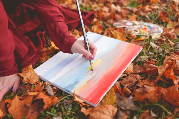 Artiste de jeune fille dessine une image à genoux dans un parc sur l'herbe.