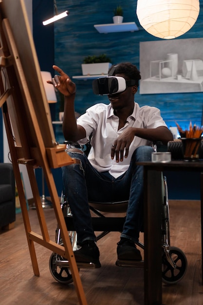 Artiste masculin afro-américain en fauteuil roulant visualisant des références d'art numérique dans le métaverse pour dessiner. Jeune étudiant en art à la recherche d'inspiration dans l'univers virtuel avec des lunettes vr.