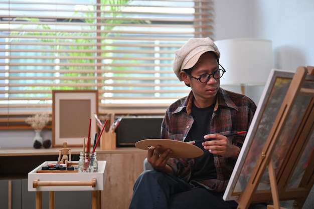 Artiste masculin peignant sur toile avec de l'eau de couleur à la maison.