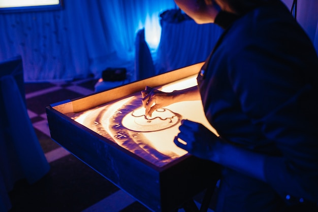 L'artiste peint des tableaux avec du sable sur une table éclairée