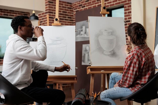 Artiste peintre femme travaillant à la technique d'esquisse avec un collègue pendant une leçon d'art dans un studio de créativité. Modèle de vase de dessin d'équipe diversifiée à l'aide d'un crayon graphique. Concept de résolutions du nouvel an