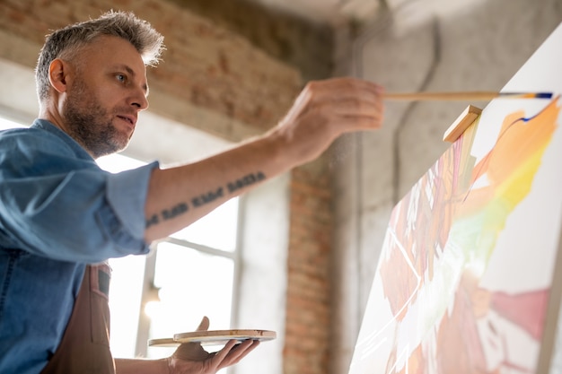 Artiste sérieux se concentrant sur la peinture d'un nouveau chef-d'œuvre tout en se tenant devant un chevalet pendant le travail