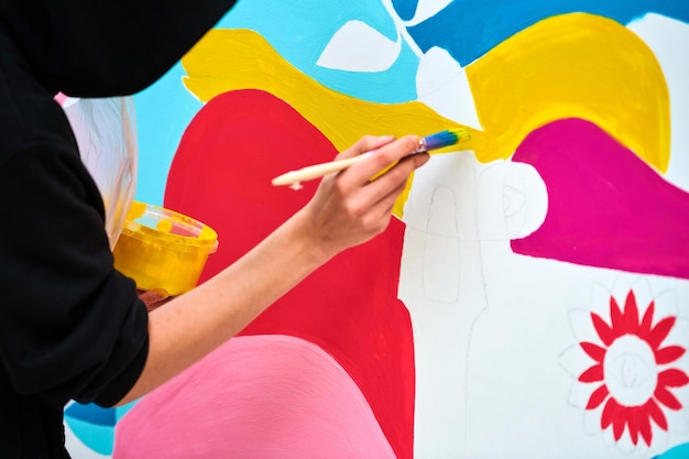 Artiste en sweat à capuche noir peignant une image colorée sur une toile blanche au festival d'art en plein air Le peintre dessine une image abstraite avec un pinceau bel art avec des performances artistiques de couleurs rouge rose et bleu