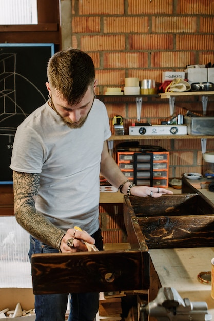 Artiste tatoué appliquant de la peinture au vernis sur un meuble en bois à l'atelier d'artisanat