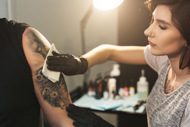 Artiste tatoueur professionnel essuyant le tatouage fini avec une serviette hygiénique dans le salon, gros plan