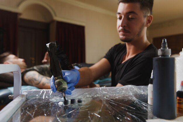 Un artiste tatoueur professionnel faisant un tatouage sur le bras d'un jeune homme par machine avec de l'encre noire