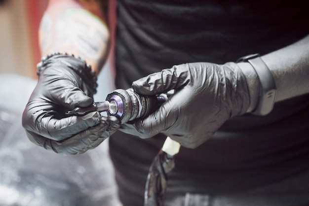 Artiste tenant une machine à tatouer dans son atelier, il est prêt à accepter le client