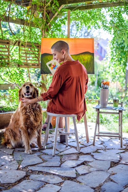 L'artiste travaille sur sa peinture à l'extérieur dans son jardin avec un golden retriever qui lui fait compagnie