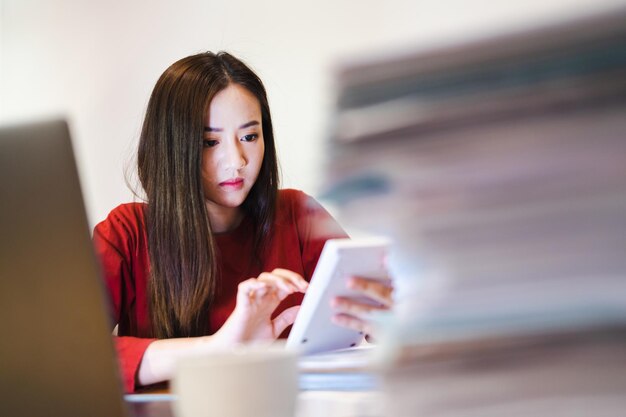 Asian Female Accountant à l'aide d'une calculatrice pendant les heures supplémentaires la nuit