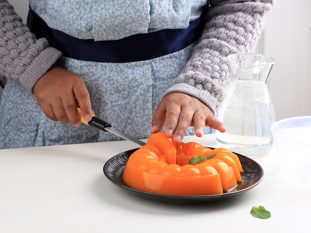 Asian Female Hand Slicing Orange Mango Pudding dans la cuisine.