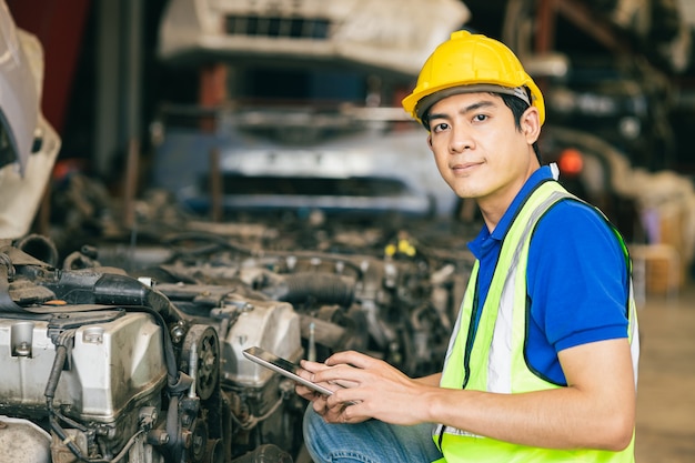 Asian Male Engineer Worker Working usign tablet pour vérifier l'ancien moteur de voiture d'occasion.