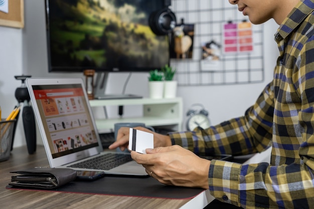 Asian man holding carte de crédit et taper des informations sur internet avec un ordinateur portable à la maison