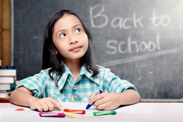 Asiat étudiante dessinant sur du papier blanc avec des crayons colorés dans la salle de classe