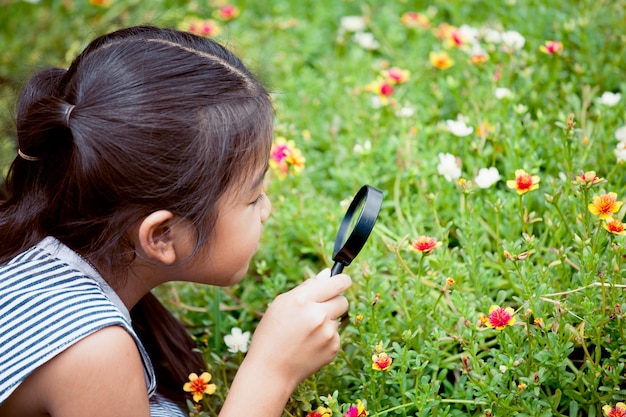 Asiat petite fille regardant à travers une loupe sur une belle fleur dans le jardin