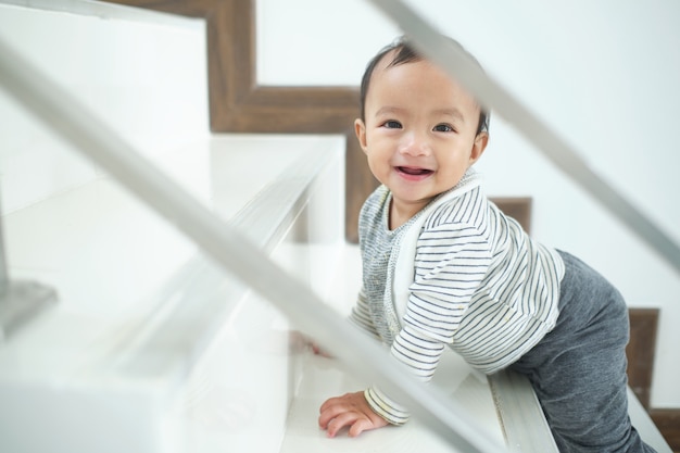 Asiatique 10 mois enfant en bas âge bébé fille enfant grimper les escaliers à la maison seul, regardant et souriant. Mouvement, équilibre et coordination, concept de jalon