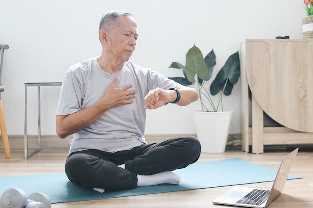 Un Asiatique âgé vérifie le rythme cardiaque sur une montre de sport après s'être entraîné à la maison.