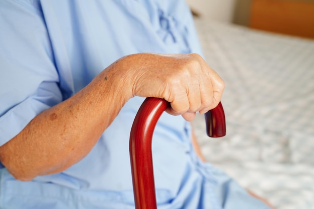 Asiatique âgée handicapée patiente tenant un bâton de marche dans la main ridée à l'hôpital
