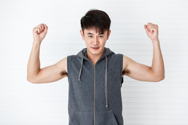 Asiatique bel homme souriant en forme tenant les mains vers le haut et serré portant des vêtements de sport gris t-shirt sans manches sur fond blanc.
