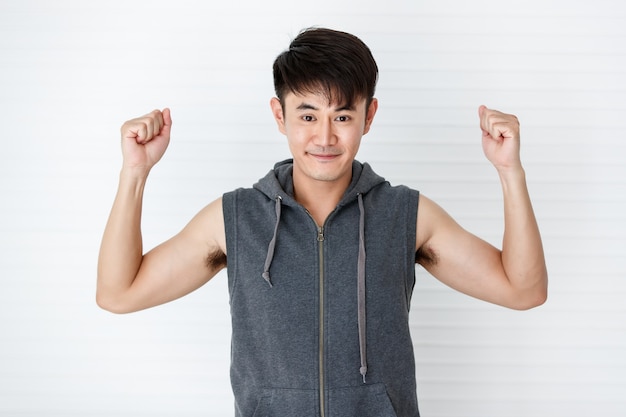 Asiatique bel homme souriant en forme tenant les mains vers le haut et serré portant des vêtements de sport gris t-shirt sans manches sur fond blanc.