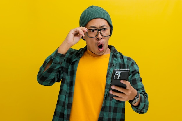 Un Asiatique choqué ajuste ses lunettes tout en regardant son smartphone avec une expression surprise.