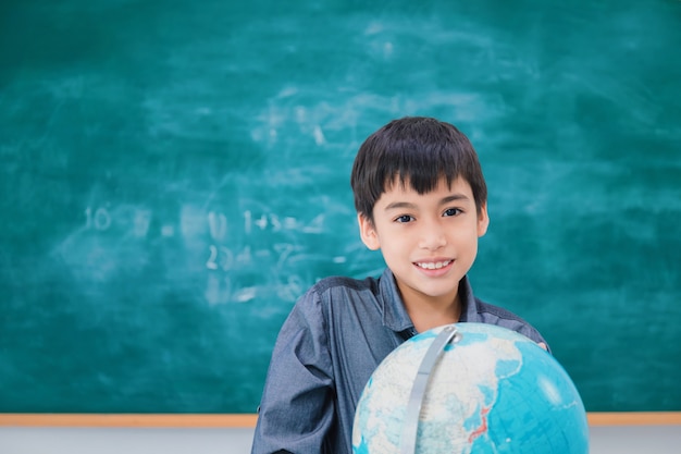 Asiatique écolier Souriant Et Réfléchissant Avec Globe Sur Tableau Noir