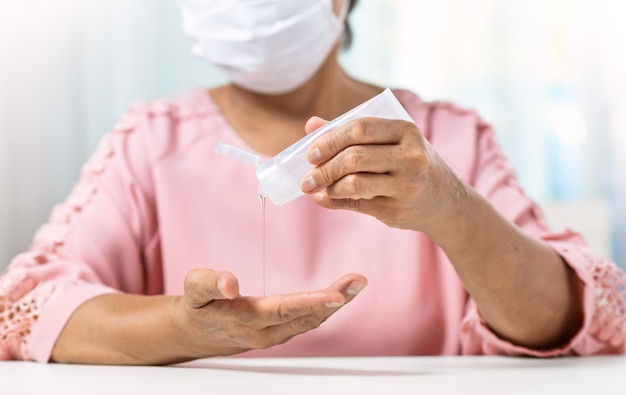 Asiatique femme âgée porter un masque chirurgical en chemise rose versant un gel portable désinfectant pour les mains sur ses paumes et ses mains pour prévenir et protéger les coronavirus ou Covid-19.