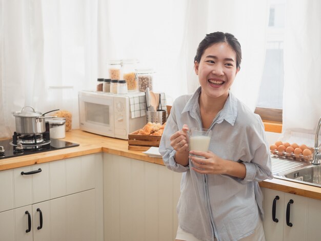 Asiatique femme boit du lait dans la cuisine