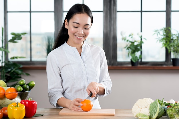 Asiatique femme coupe orange sur une planche à découper en bois dans la cuisine