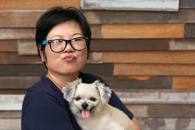 Asiatique femme étreignant le chien si mignon avec un mur en bois