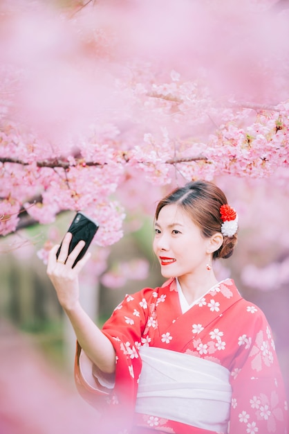 Asiatique femme portant un kimono à l&#39;aide d&#39;un smartphone avec des fleurs de cerisier, sakura au Japon.