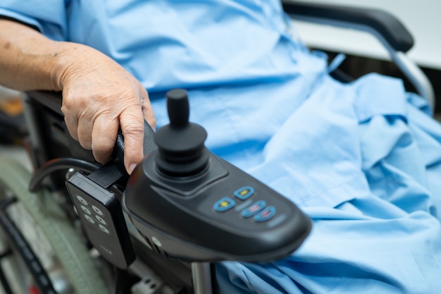 Asiatique femme senior patient sur fauteuil roulant électrique avec télécommande à l'hôpital.