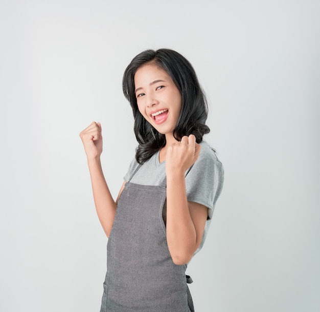 Asiatique femme en tablier et debout avec étonné de succès et impatient sur fond gris