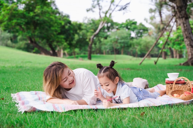 Photo asiatique grand-mère et petite-fille portant sur le champ de verre vert en plein air, famille profitant de pique-nique ensemble en jour d'été