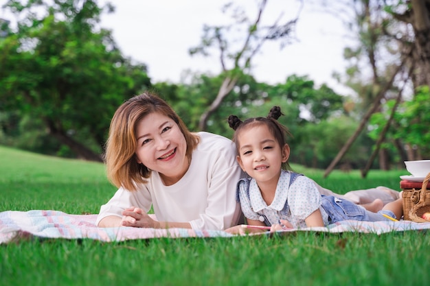 Photo asiatique grand-mère et petite-fille portant sur le champ de verre vert en plein air, famille profitant de pique-nique ensemble en jour d'été