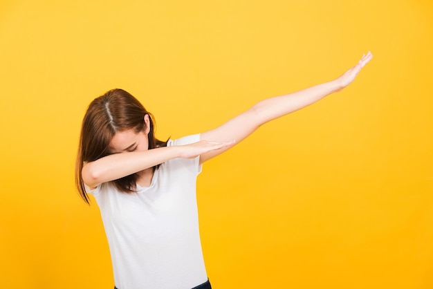 Asiatique heureux portrait belle jolie jeune femme adolescent sourire debout porter t-shirt mouvement montrant DAB danse contre geste isolé, studio tourné sur fond jaune avec espace de copie