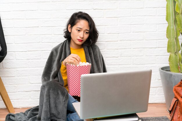 Asiatique jeune femme assise sur le sol en mangeant des popcorns