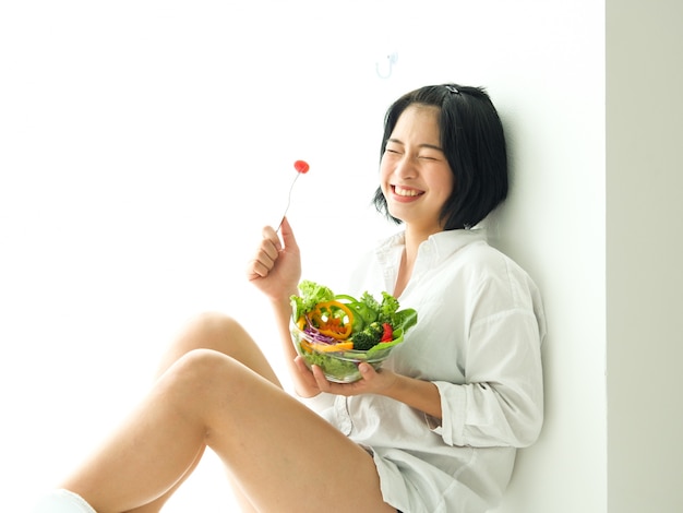 Asiatique jeune femme eatiing salade sur fond blanc régime alimentaire