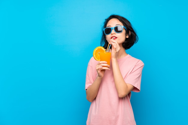 Asiatique jeune femme sur un mur bleu isolé, tenant un cocktail