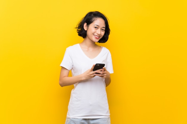 Asiatique jeune femme sur un mur jaune isolé, envoyant un message avec le téléphone portable