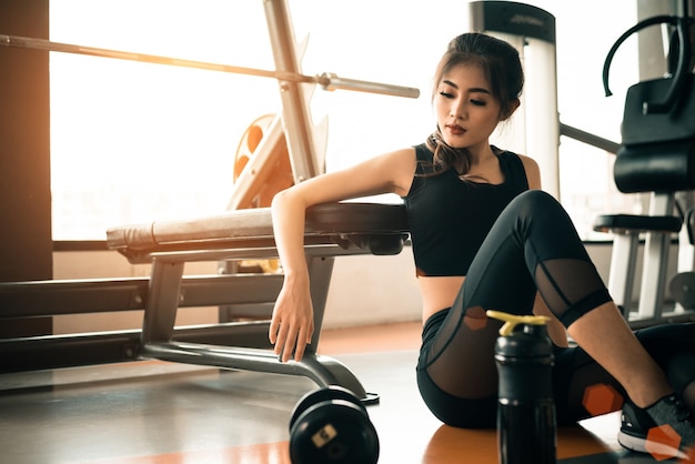 Asiatique jeune femme se détendre dans la salle de fitness et centre de sport avec équipement et haltère