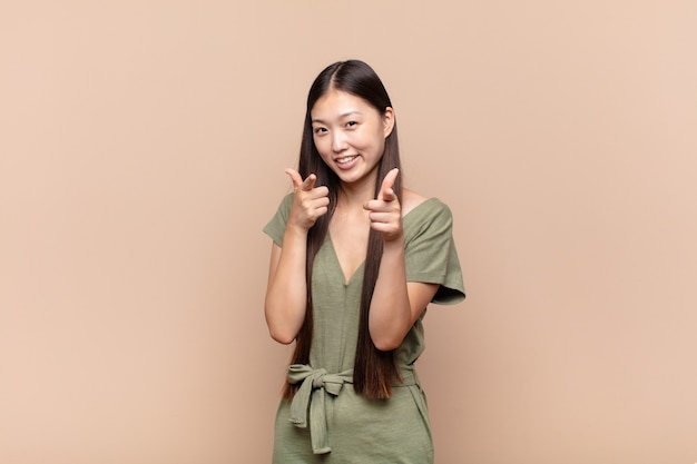 Asiatique jeune femme souriante avec une attitude positive, réussie, heureuse, pointant vers la caméra, faisant signe de pistolet avec les mains
