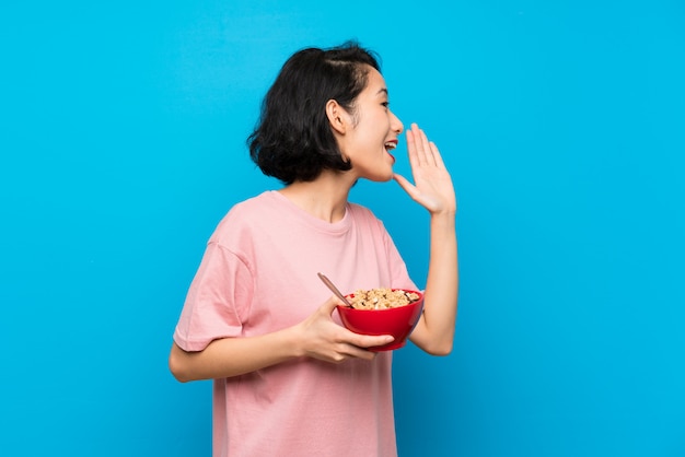 Asiatique jeune femme tenant un bol de céréales en criant avec la bouche grande ouverte