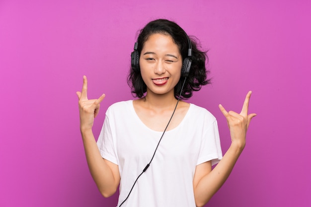 Asiatique jeune fille écoutant de la musique avec un téléphone portable sur un mur violet isolé