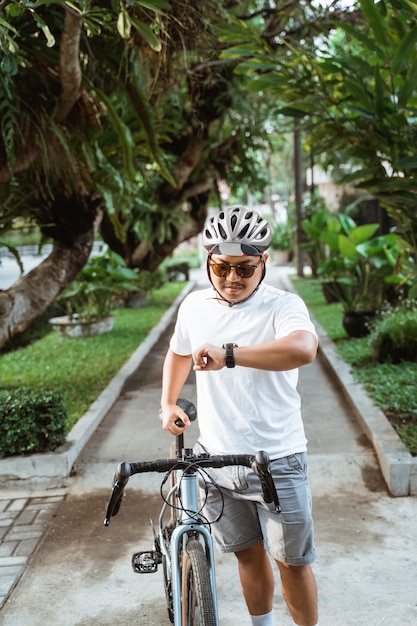 Asiatique jeune homme portant un casque à pied avec vélo de route en regardant sa montre