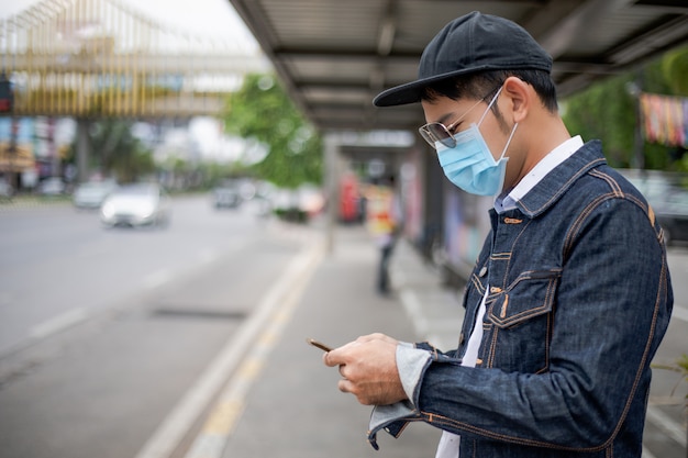 Asiatique jeune homme utilisant un téléphone intelligent dans la ville et portant un masque facial pour la protection de la pollution de l'air, des particules et pour la protection virus de la grippe, grippe, coronavirus