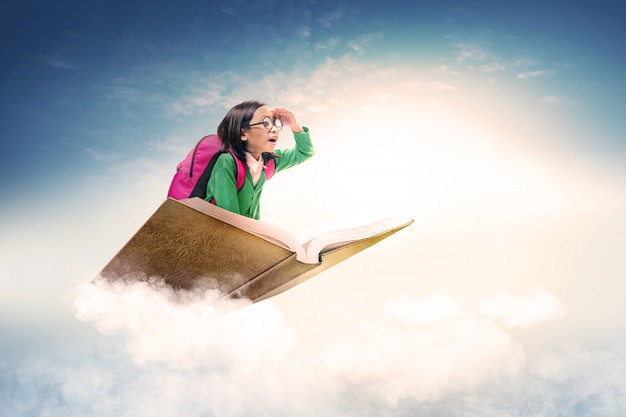 Asiatique jolie fille avec des lunettes et sac à dos, assise sur le livre avec un ciel bleu